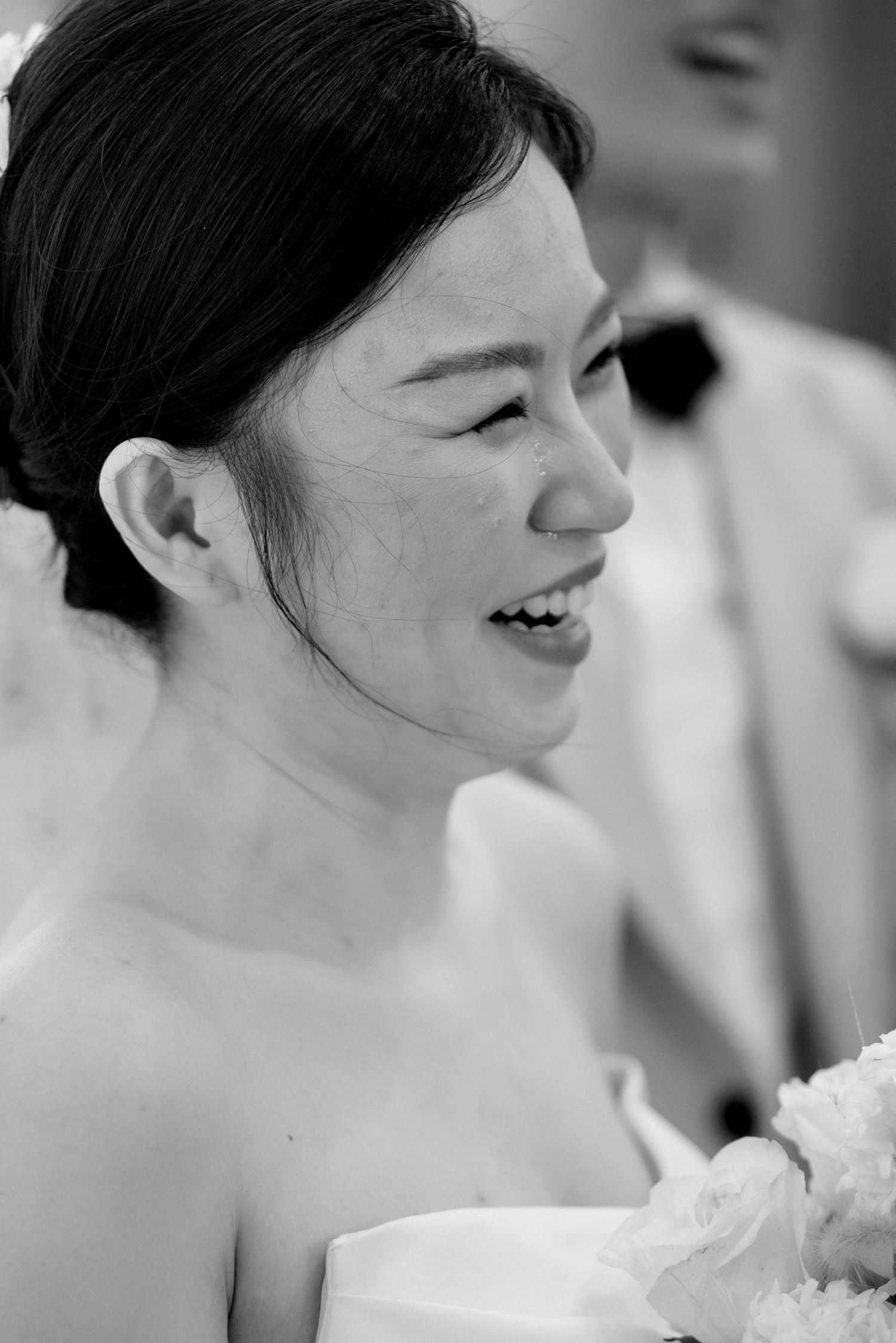 Radiant bride smiles warmly in close-up black and white wedding portrait with bouquet.
