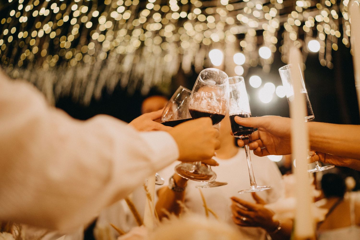 Wedding guests clink glasses in a celebratory toast under sparkling string lights at night.