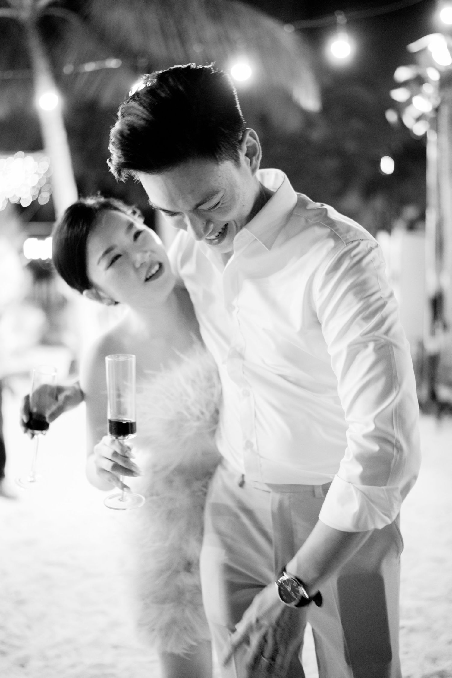 Black and white photo of laughing bride and groom sharing a joyful moment at reception.