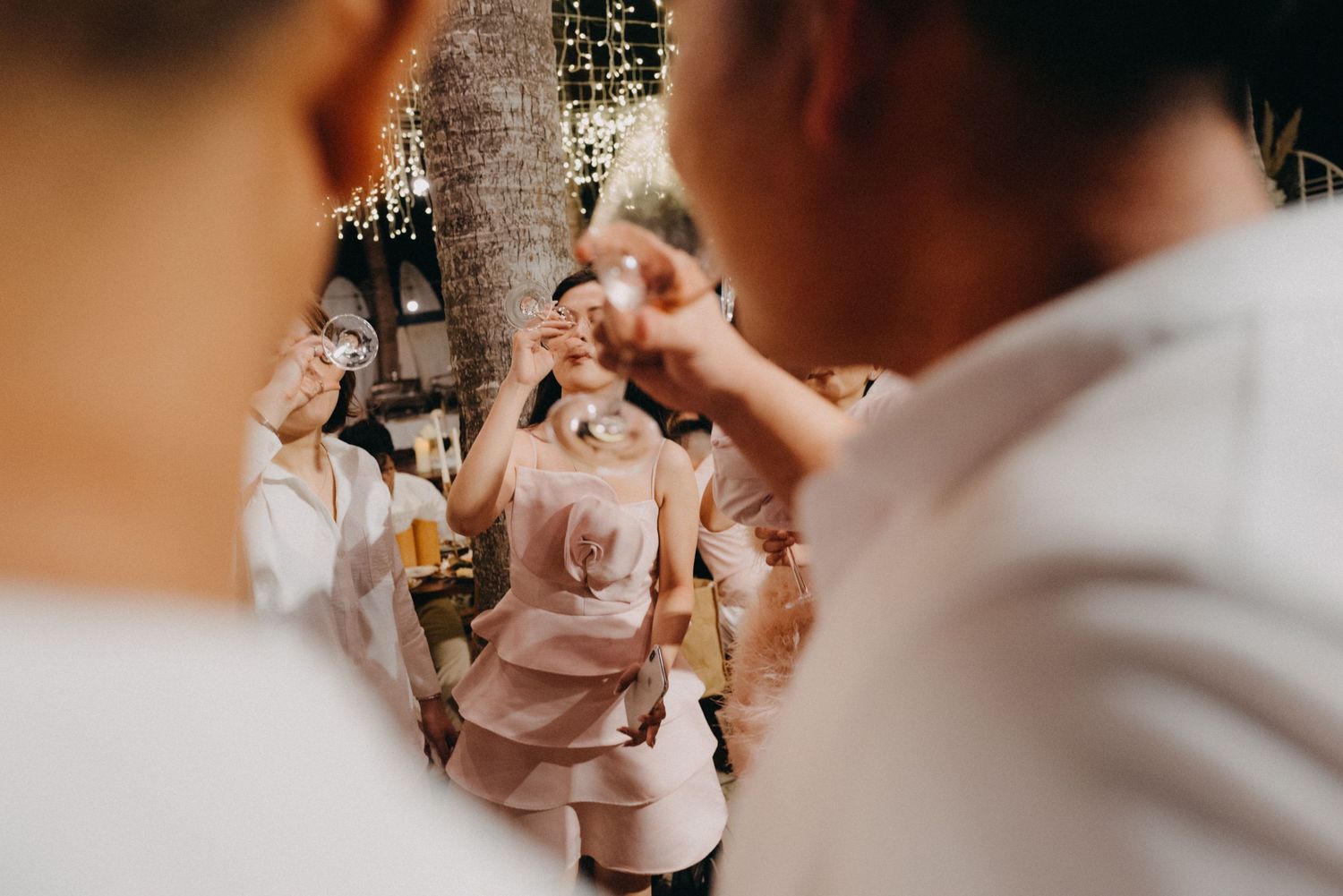 Group of guests toasting drinks at an outdoor wedding reception with warm lighting.