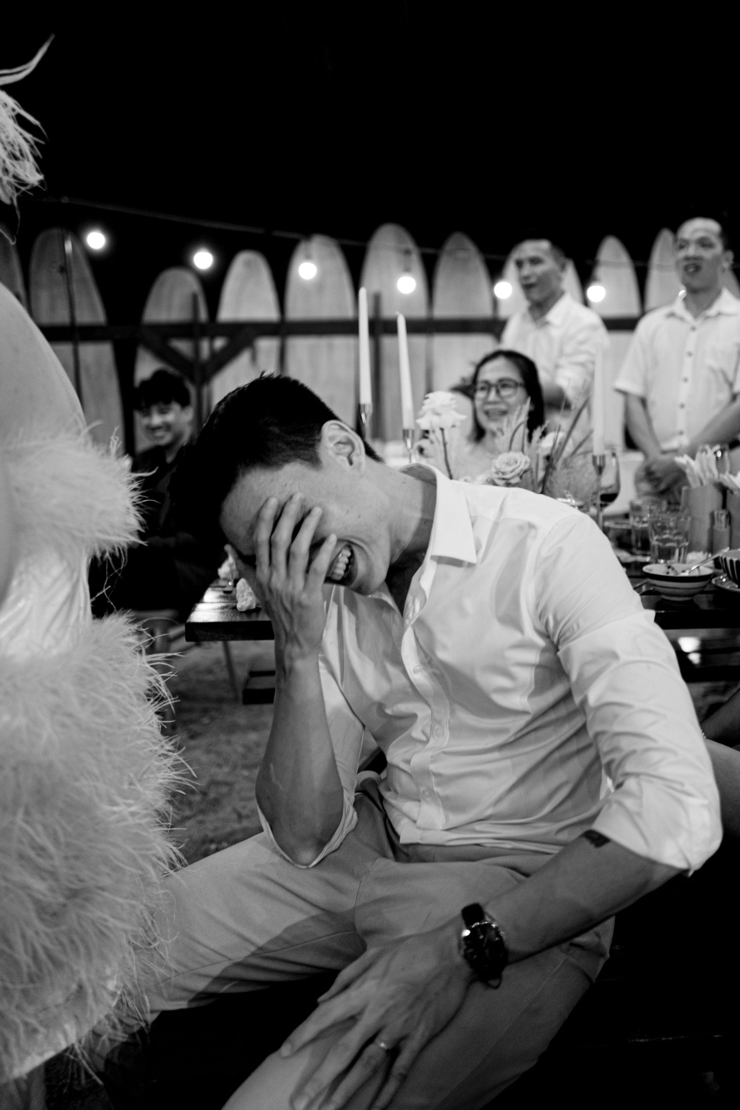 Emotional groom covering face with hand while laughing at outdoor wedding reception.