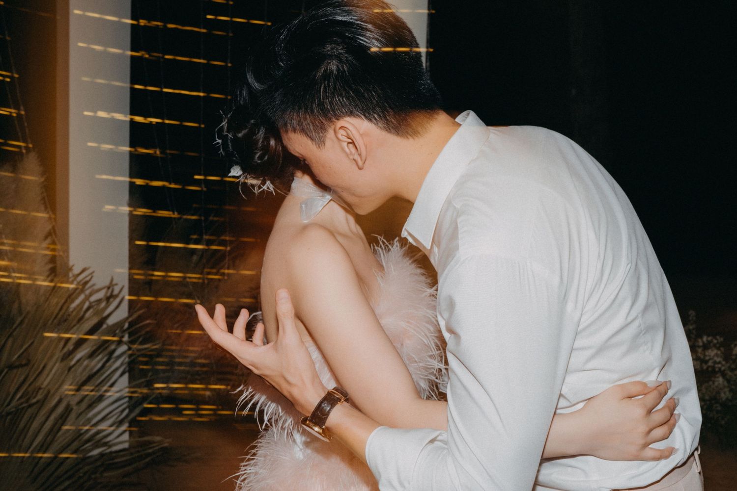 Romantic couple in intimate embrace, woman in pink feather dress and man in white shirt at night event.