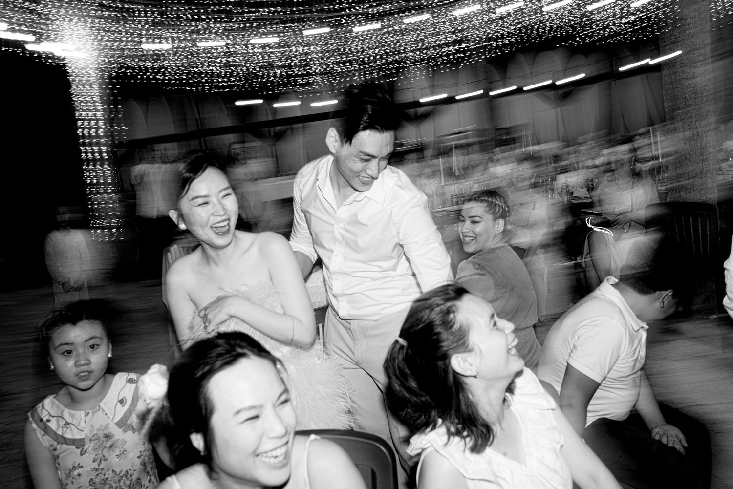 Black and white candid photo of laughing wedding guests seated and socializing at festive reception.