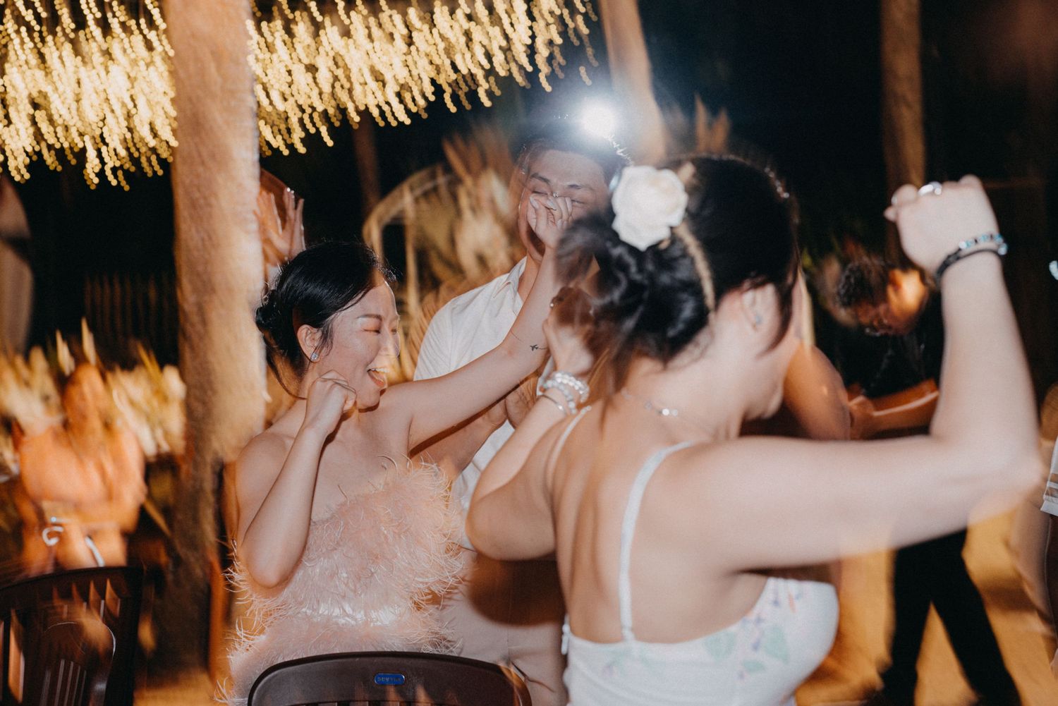 Bride in white dress embracing female guests during joyful dancing at outdoor wedding celebration.