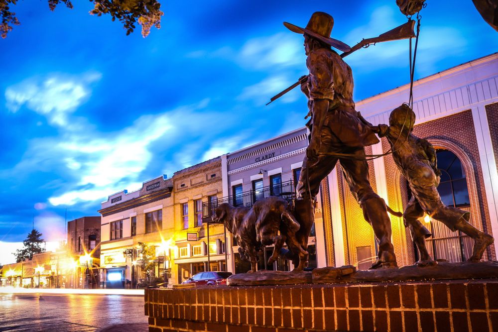 Bronze statue silhouettes against vibrant blue sky in downtown setting at dusk.