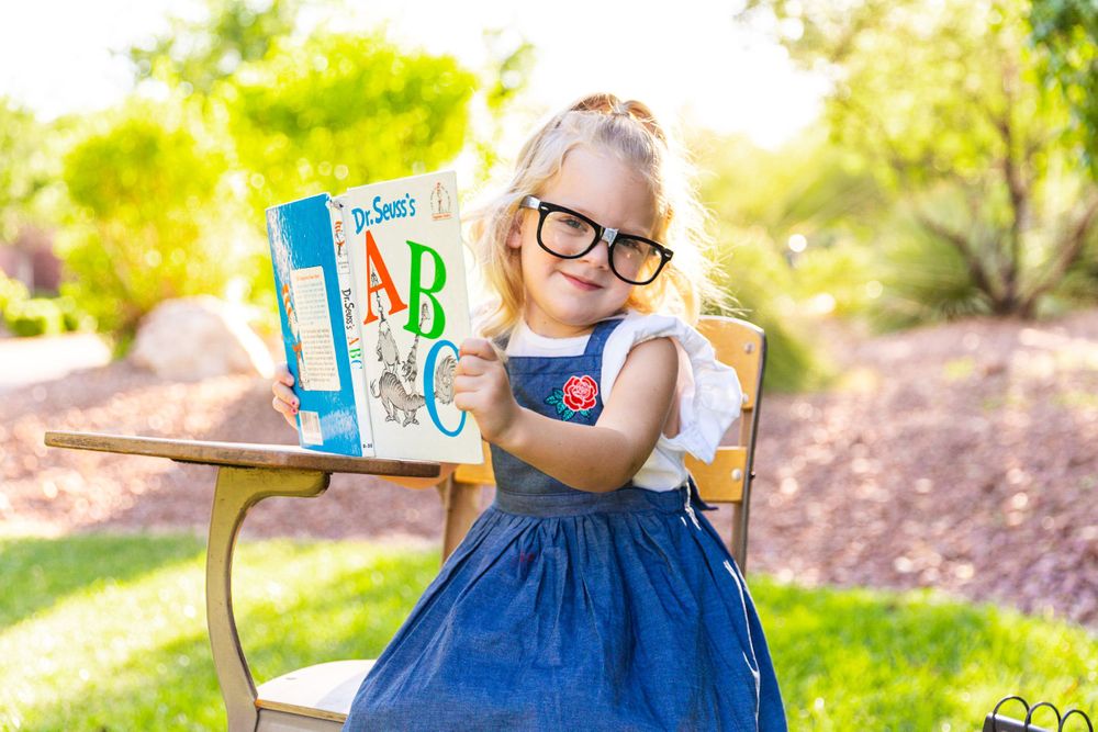 Student showing ABC books while sitting at a vintage desk outdoors.