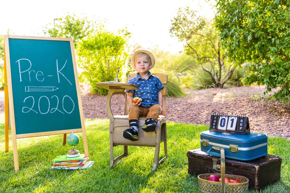 Back to school photo setup with chalkboard, vintage desk and stacked suitcases in a garden.