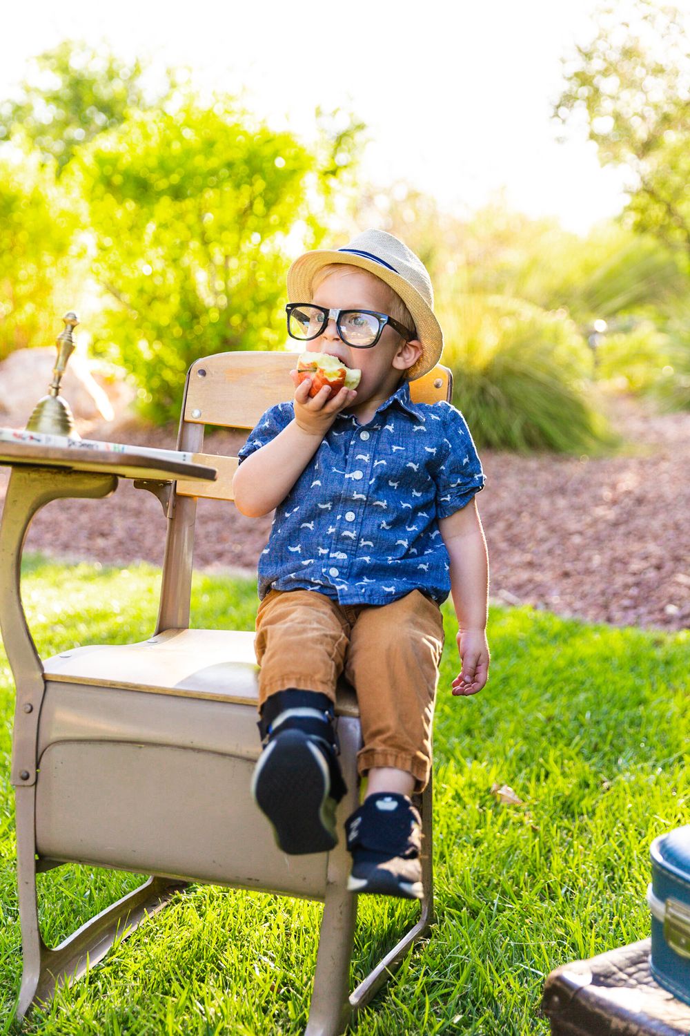 A student sits at an outdoor desk enjoying a snack while wearing a blue shirt and glasses.