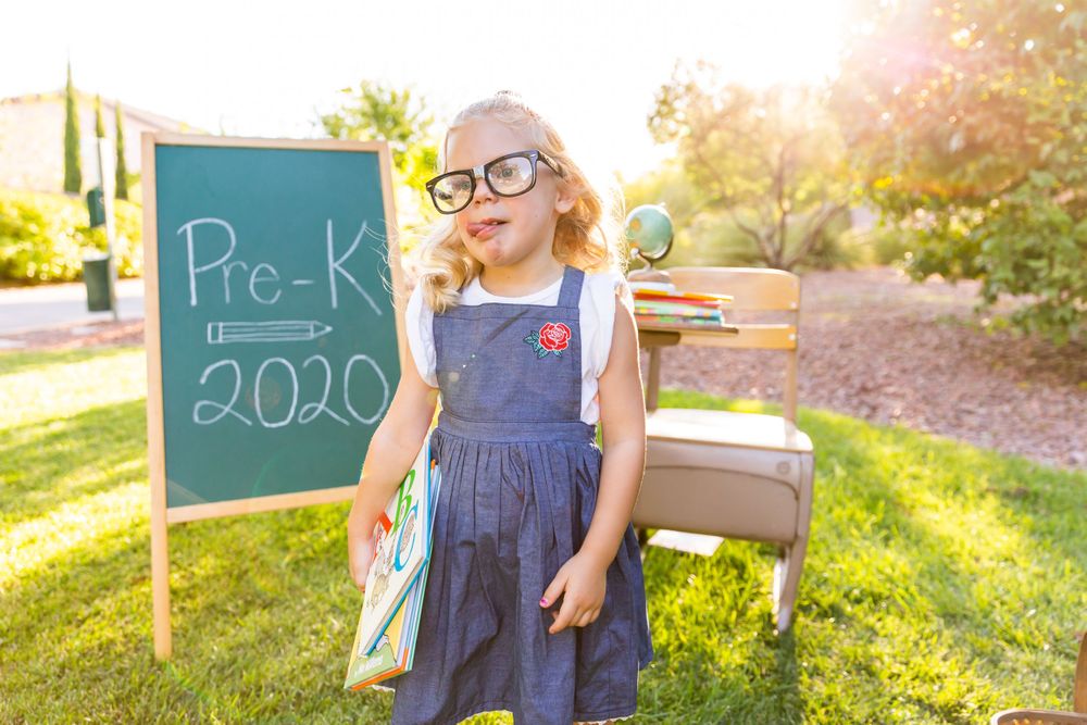 A back to school photo setup with a chalkboard showing Pre-K 2020 in an outdoor garden setting.