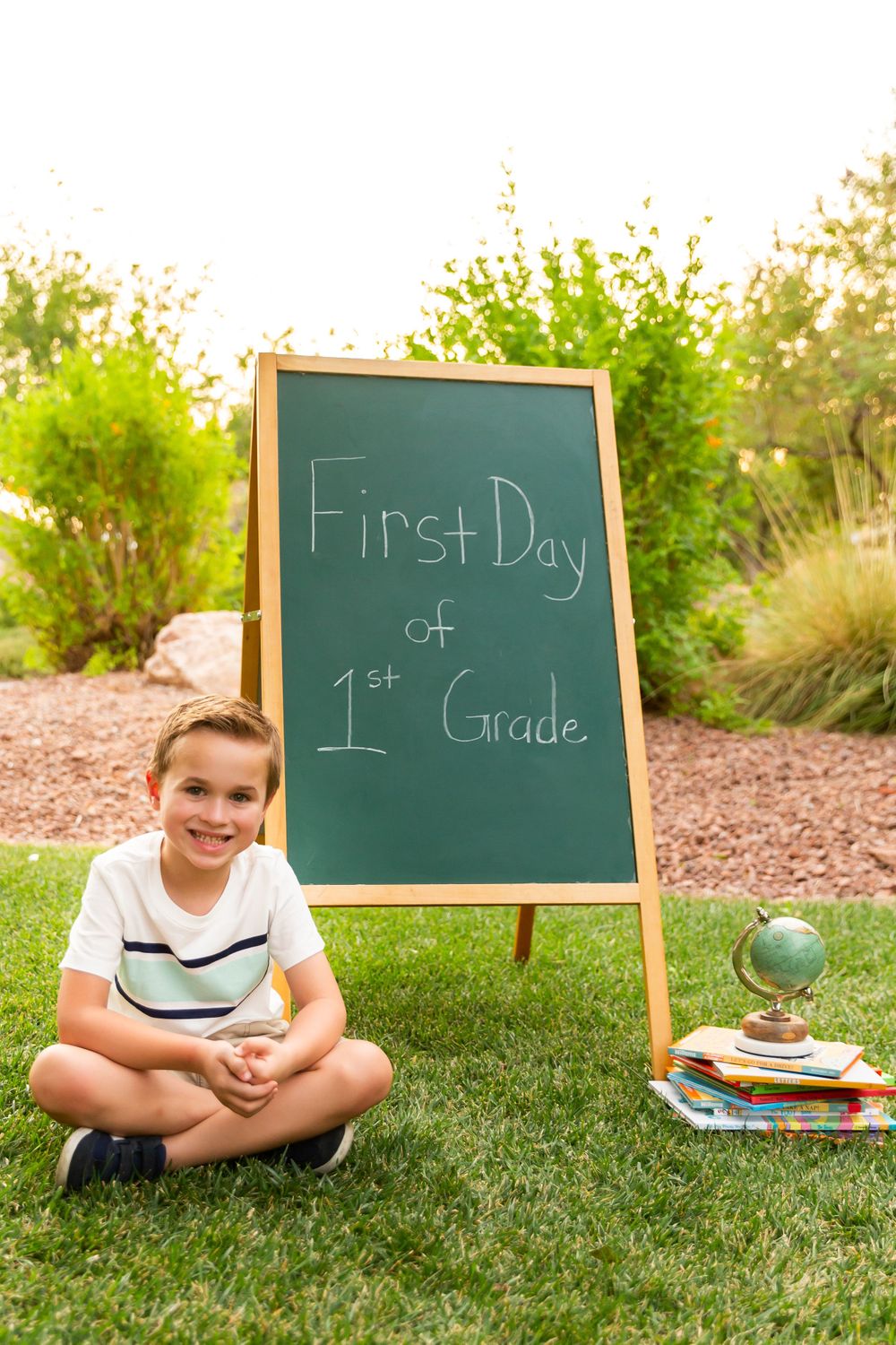 First day of school photo with chalkboard sign and educational props on grass.