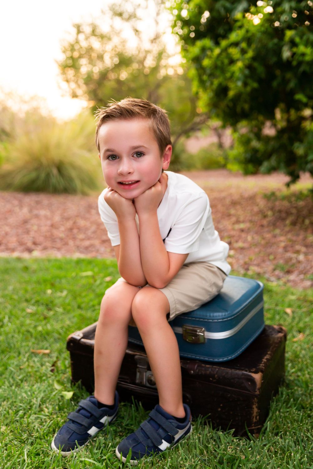 Young student sitting on vintage suitcases in garden setting.