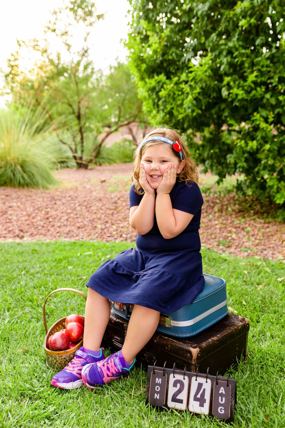 Child sitting on vintage suitcases with apples and wooden countdown blocks in a garden setting.