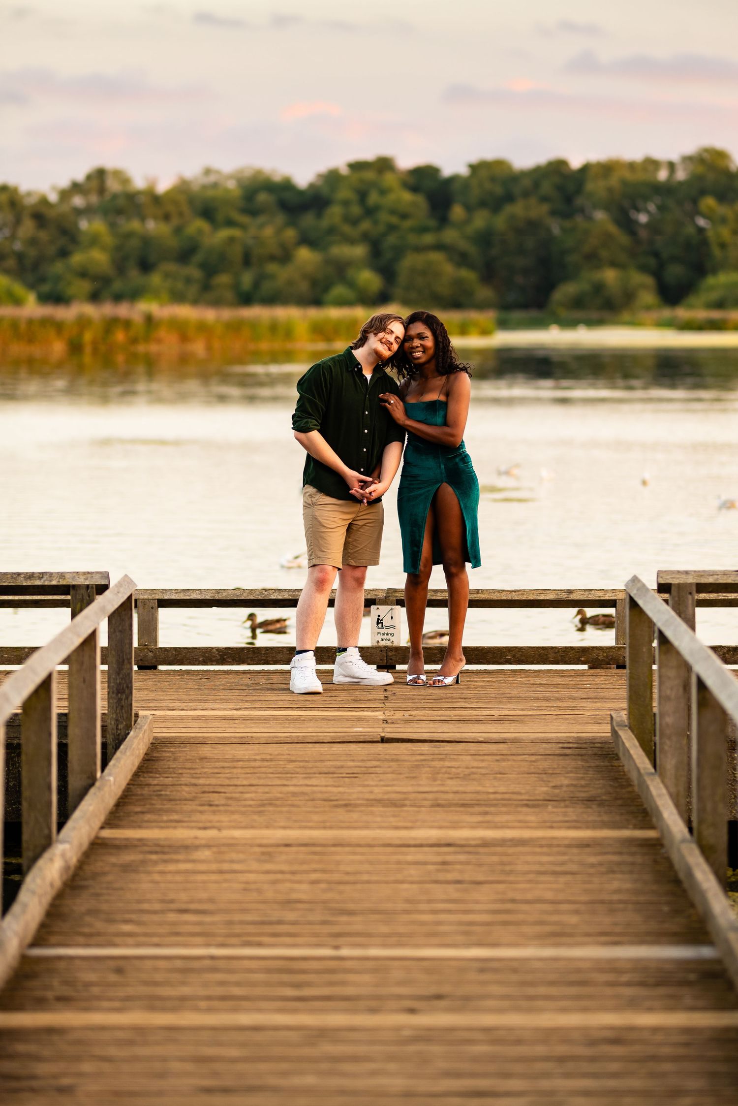 Romantic couple posing together on wooden boardwalk during sunset.