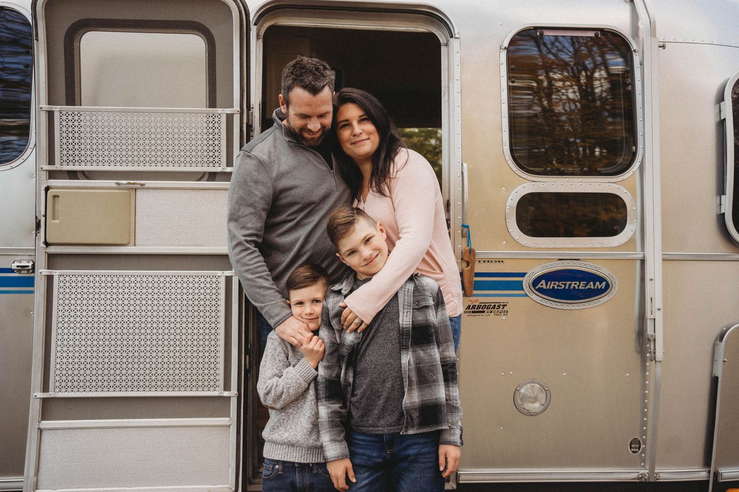Family poses together in front of vintage silver Airstream trailer on cloudy day.