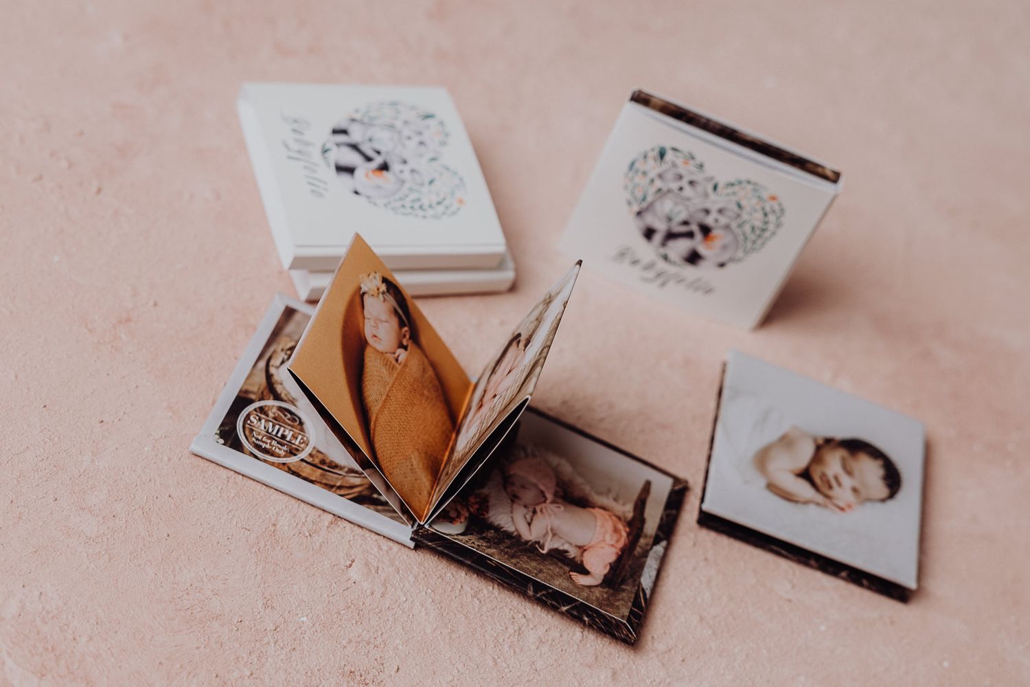 Collection of small photo books and albums arranged on a pink surface.