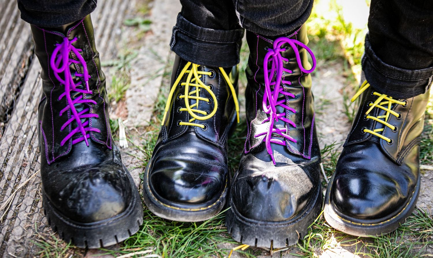 Black boots with purple and yellow laces arranged in a row on grass.