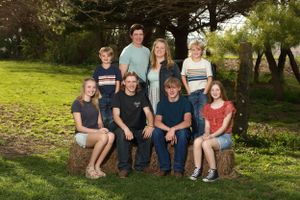 Family portrait taken outdoors on a wooden bench with trees and greenery in the background.