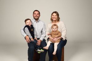Studio family portrait with parents and two young children in neutral tones.