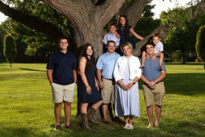 Extended family group portrait under large tree in sunny garden setting.