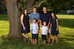 Family group portrait outdoors with large tree trunk as natural backdrop.