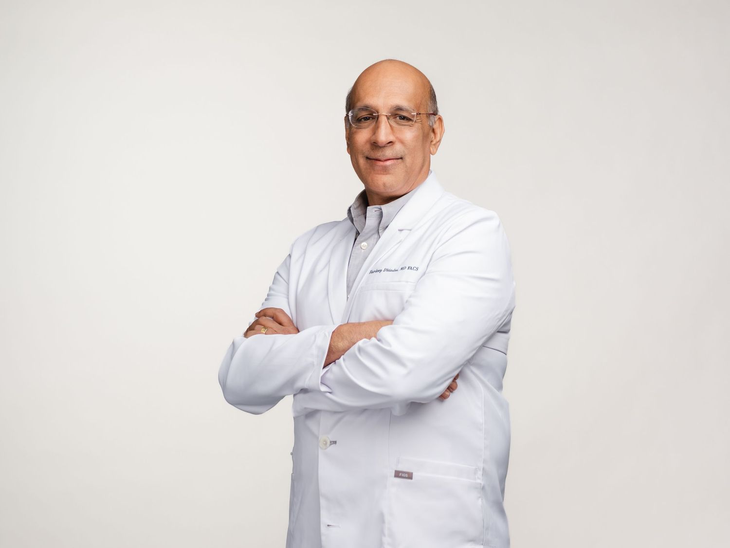 Medical professional in white lab coat standing with arms crossed against light background.