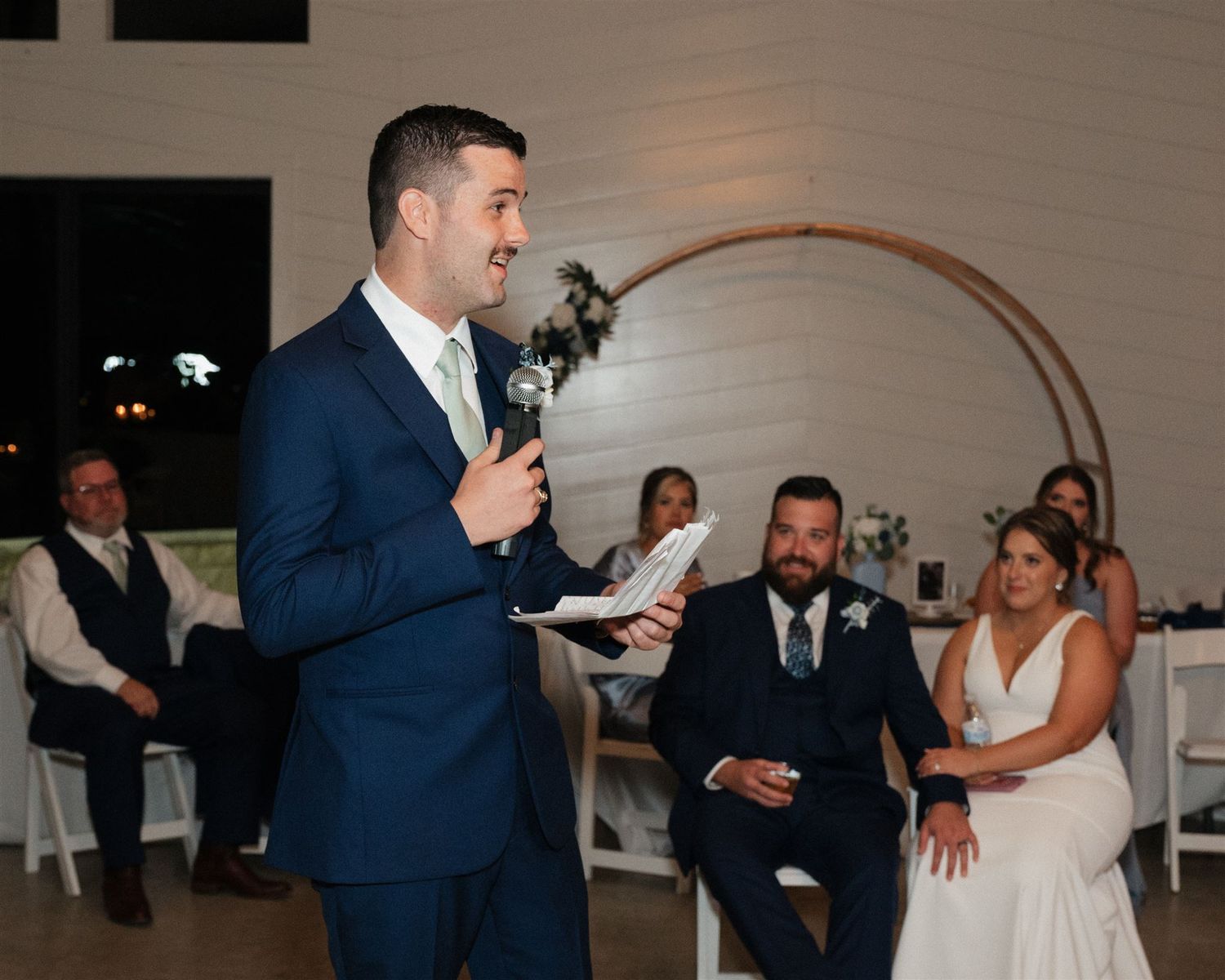 A guest delivers a wedding speech while the couple listens from their seats.