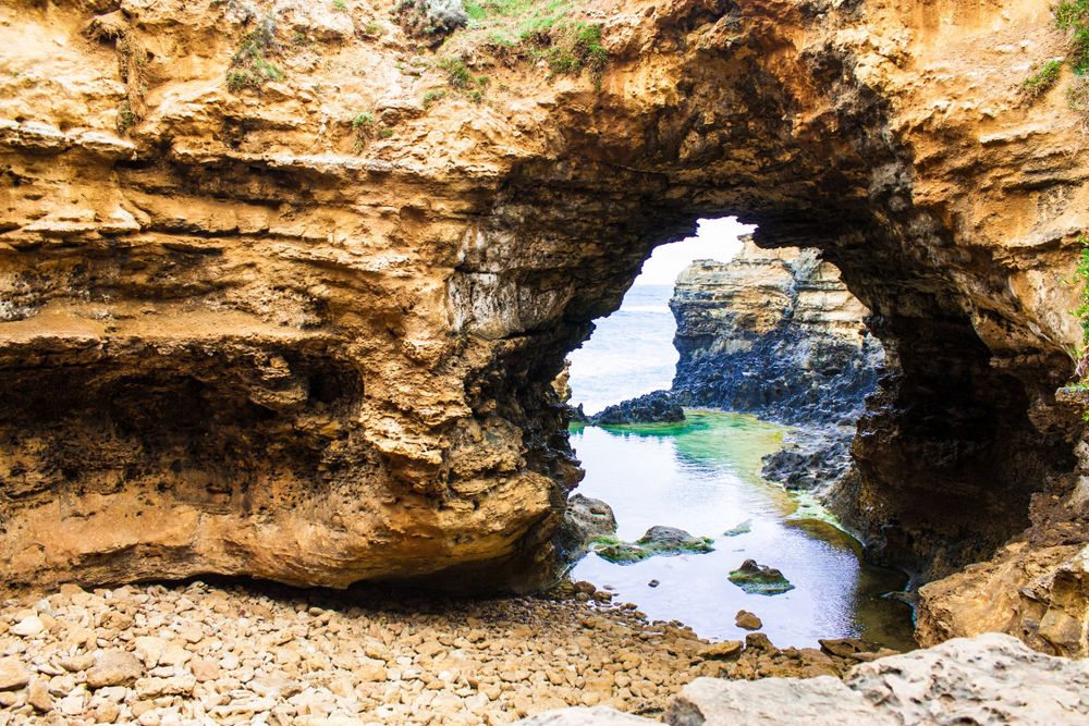 Natural stone arch formation along the coastline frames turquoise ocean waters and rocky outcrops.