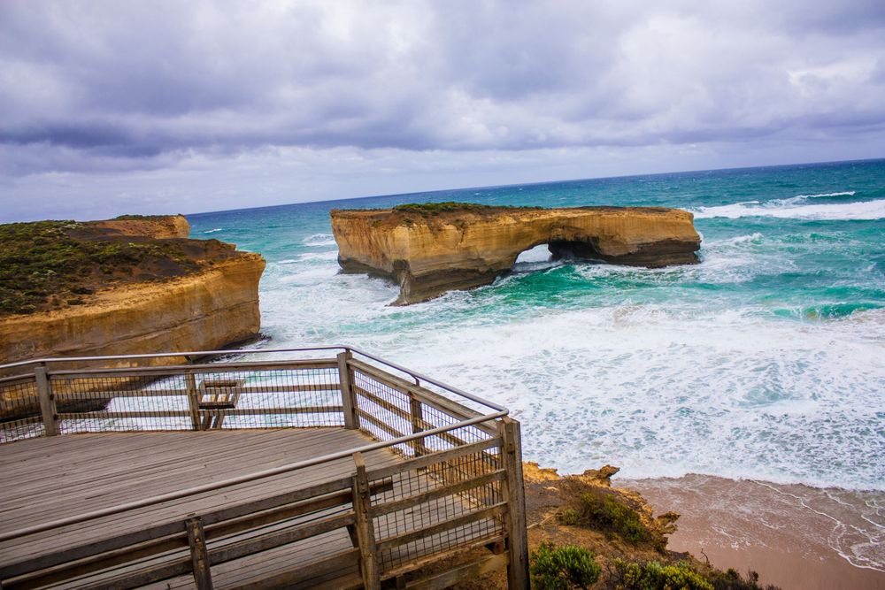 Wooden viewing platform overlooks dramatic limestone cliffs and crashing waves along the Great Ocean Road.