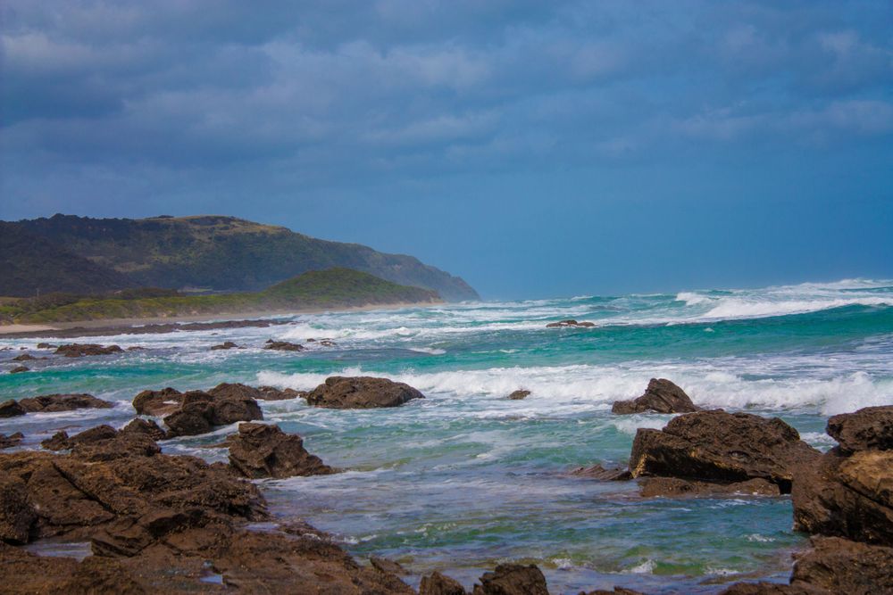 Rocky coastline with crashing turquoise waves against rugged shore under moody sky.
