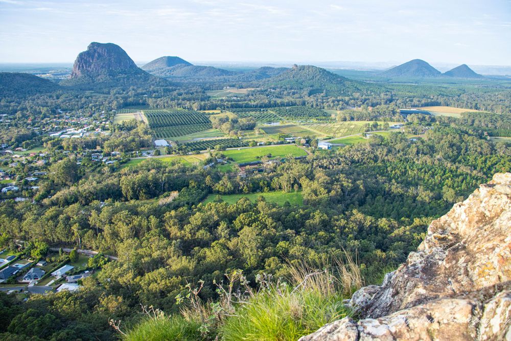 Panoramic view of Glass House Mountains with suburban development nestled in valley.