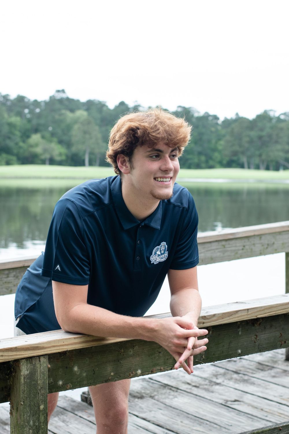 Casual outdoor portrait on a wooden dock wearing a navy polo shirt with a lake view.