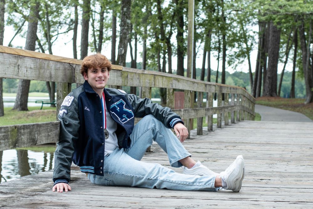 Casual portrait of someone lounging on a wooden boardwalk in a black jacket and jeans.