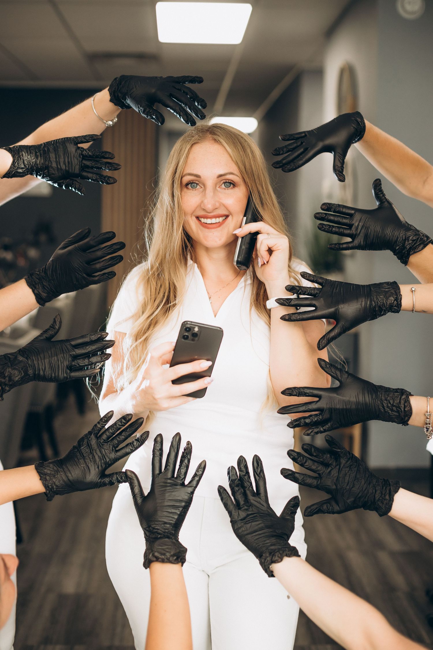 Multiple hands wearing black gloves reaching towards someone in white using a mobile phone.