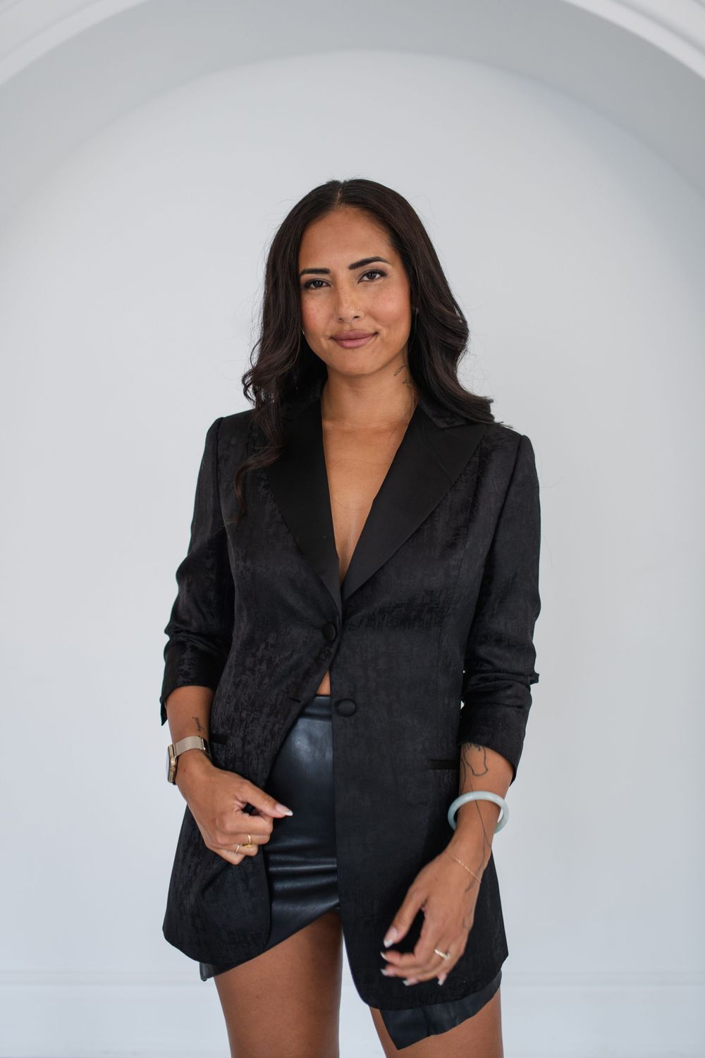 Fashion model wearing black blazer and shorts poses in white arched interior setting.