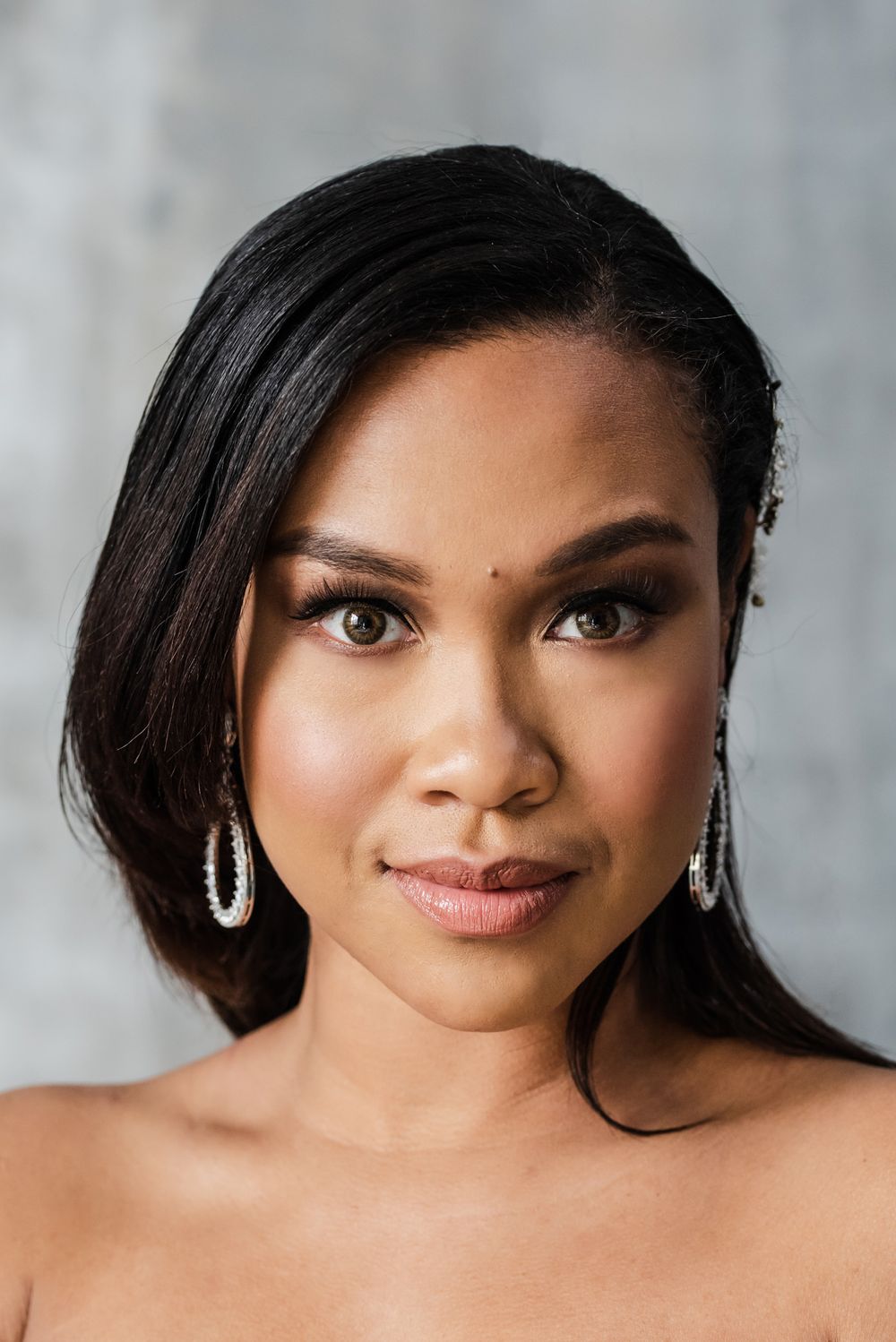 Glamorous headshot featuring sparkling earrings and evening makeup against grey background.