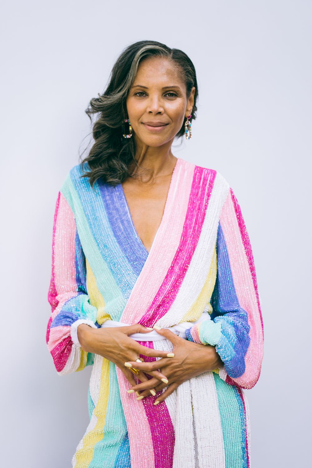 A person poses in a colorful striped sequin wrap dress with long sleeves against a white background.