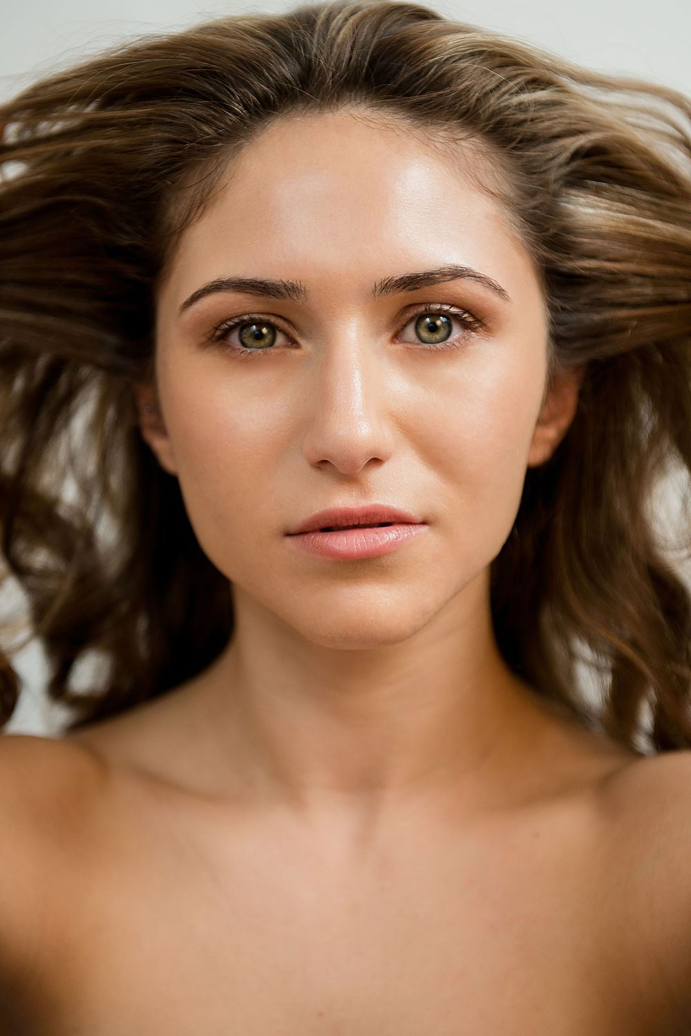 Beauty portrait of a young woman with flowing brown hair and natural makeup against light background.