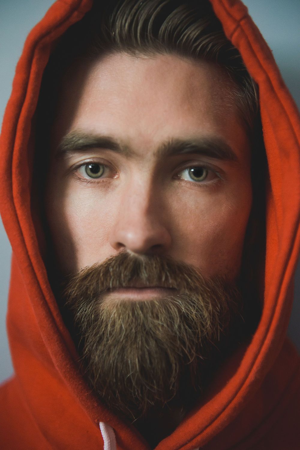 Portrait of a person wearing a red hood showcasing intense eyes and full beard.