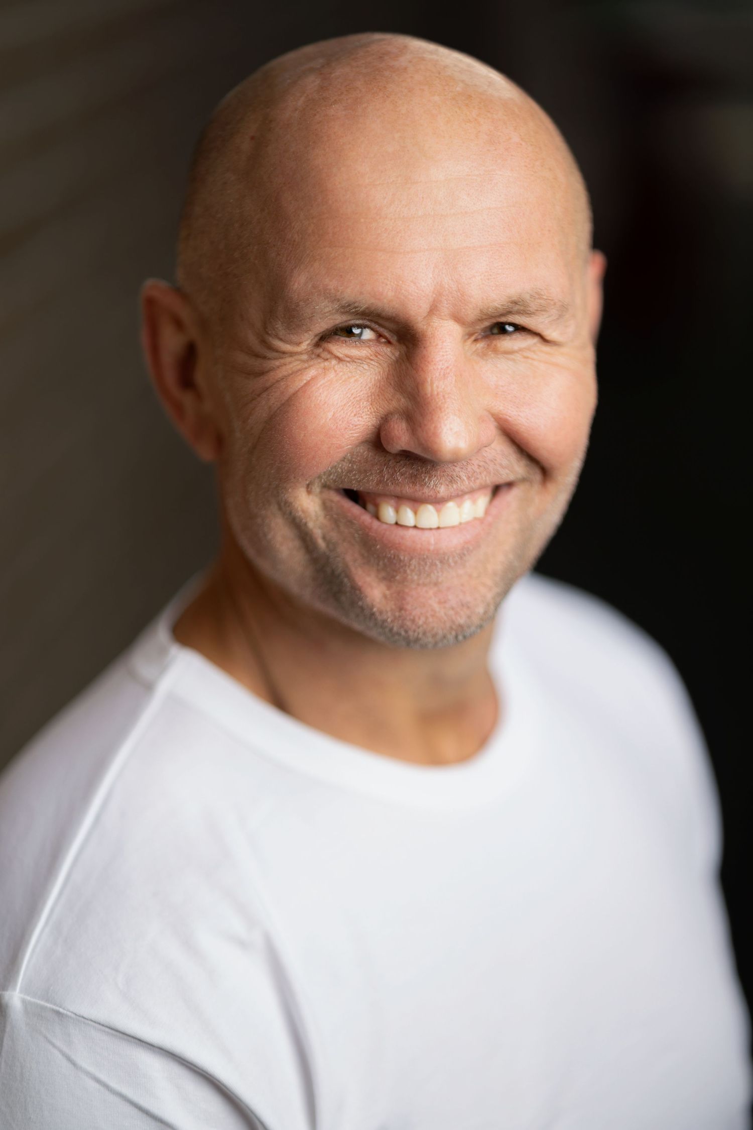 Smiling bald man in a white t-shirt, natural light headshot portrait with warm bokeh background, portrait photography