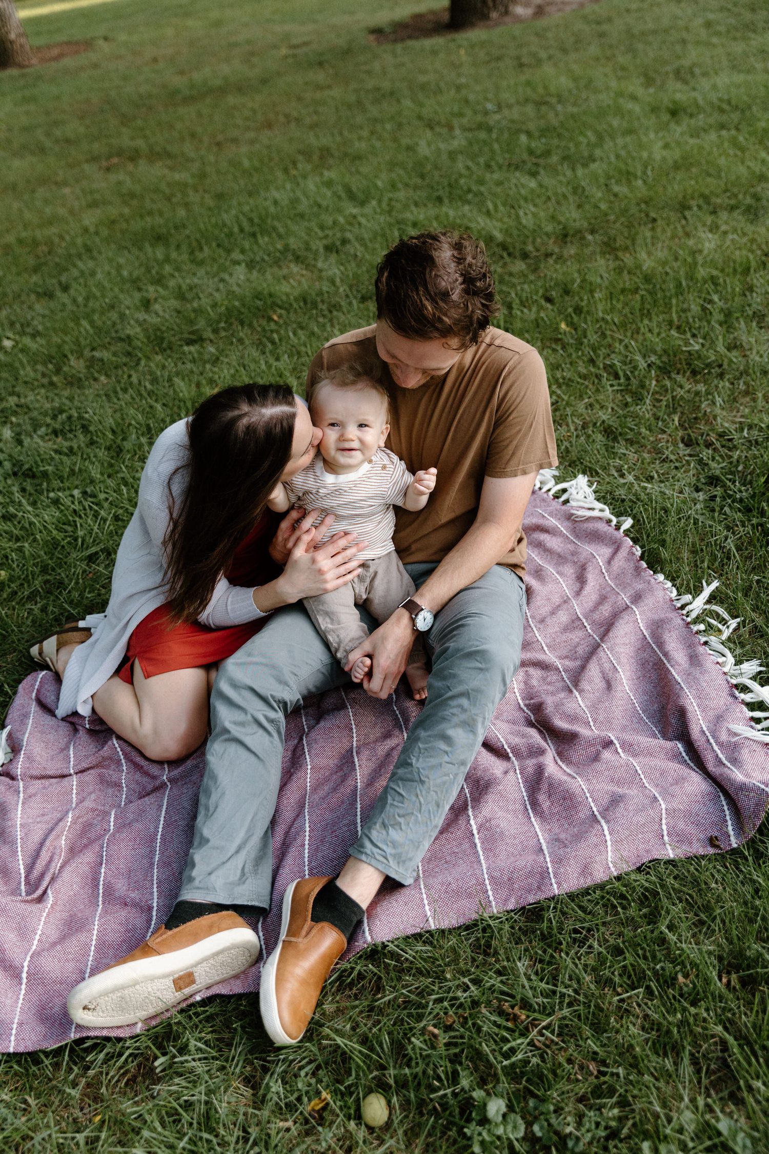 Family lounging on a purple blanket in the grass during an outdoor photo session.