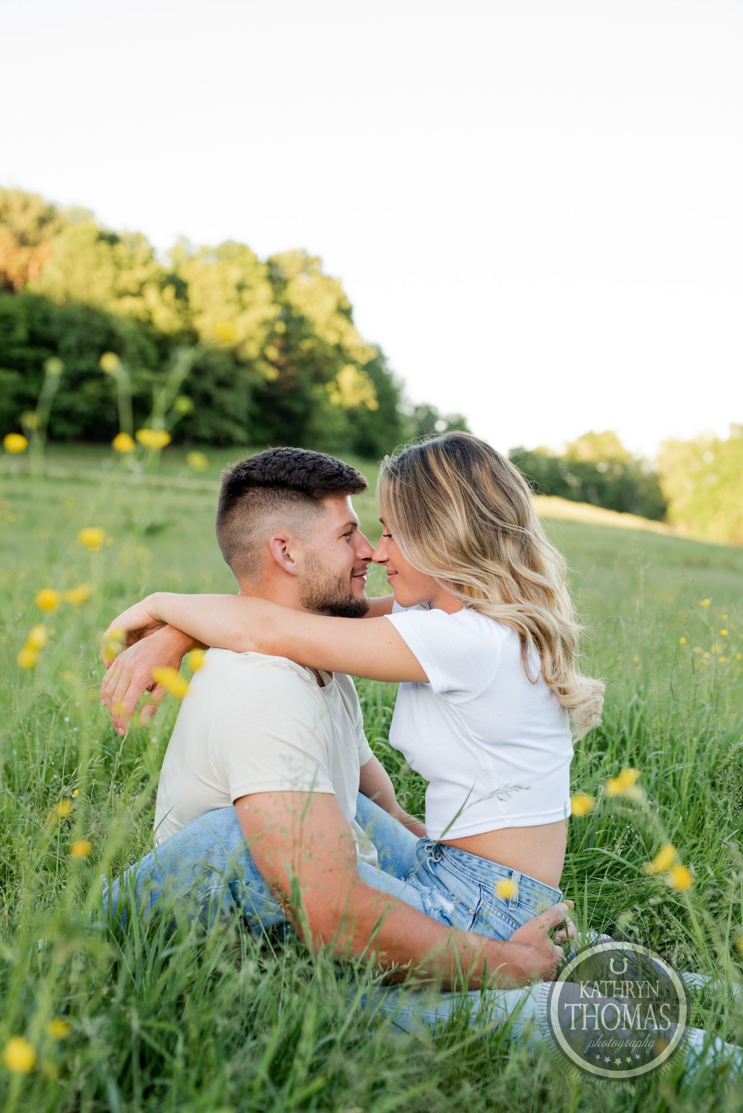 Intimate moment between couple sitting in tall grass with yellow flowers during golden hour.