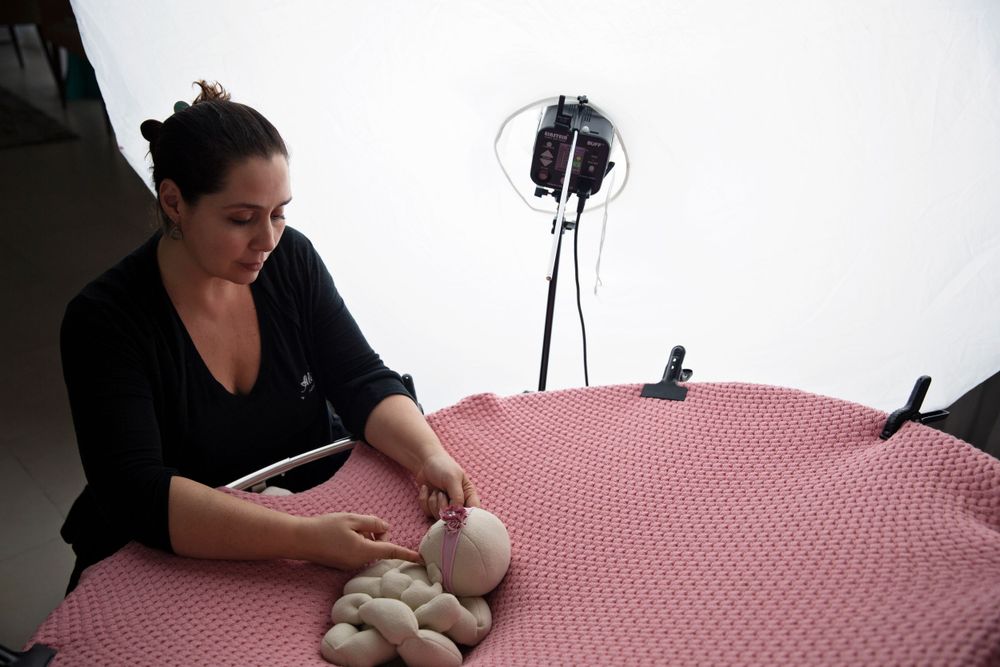 Photographer setting up newborn photo session with props on pink backdrop.
