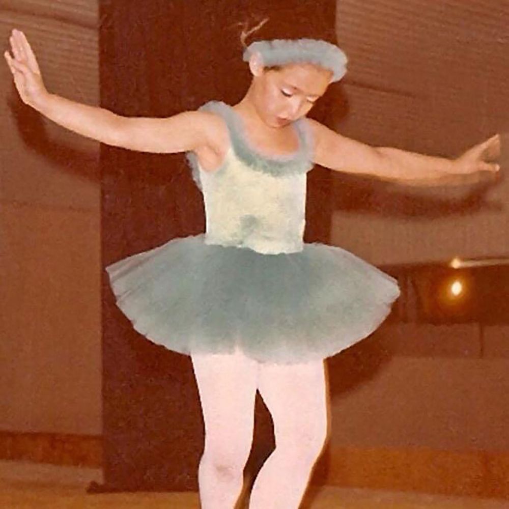 Young ballerina in pale blue tutu performs graceful pose during dance recital.