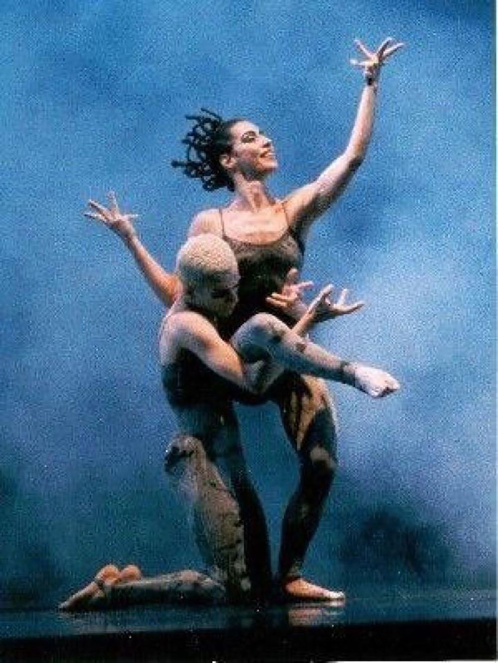 Modern ballet dancers perform dramatic lift against blue backdrop during performance.