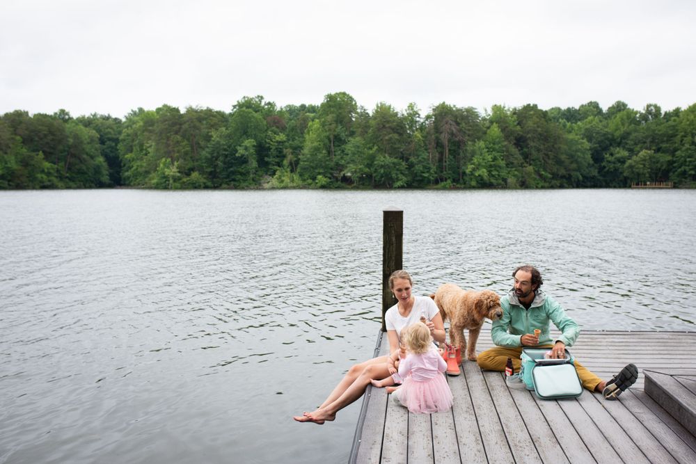 Family with dog relaxing on wooden dock by serene lake on sunny day.