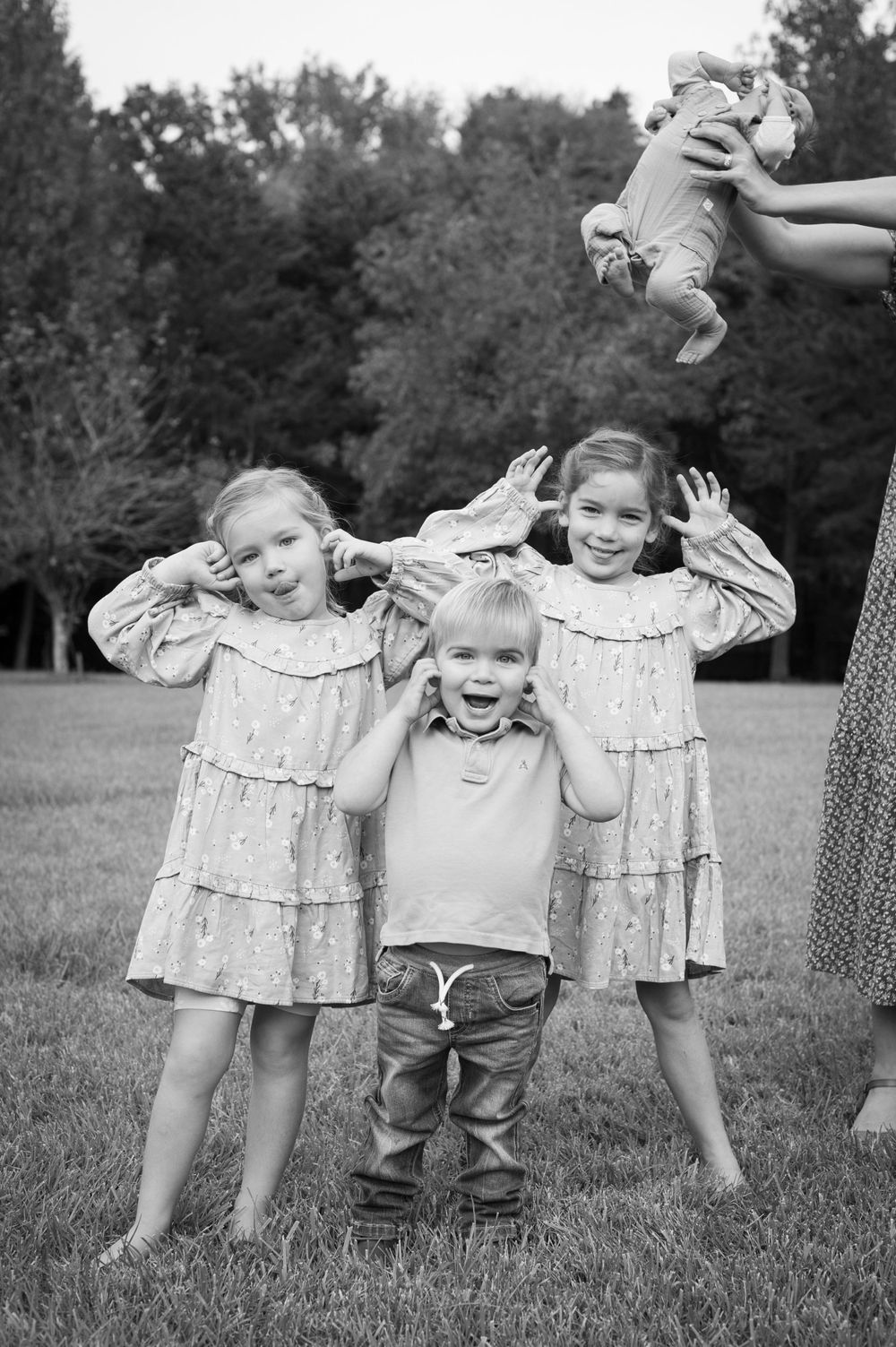 Children playing and posing while someone holds baby in air outdoors.
