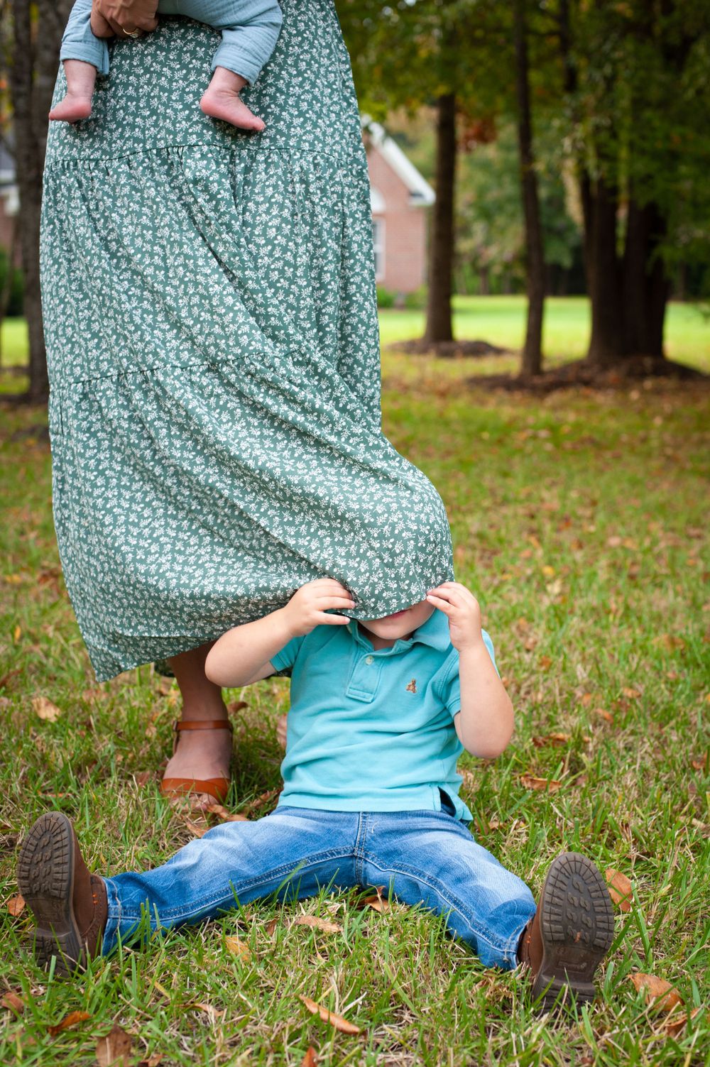 Playful moment with child hiding under floral dress in grassy yard.