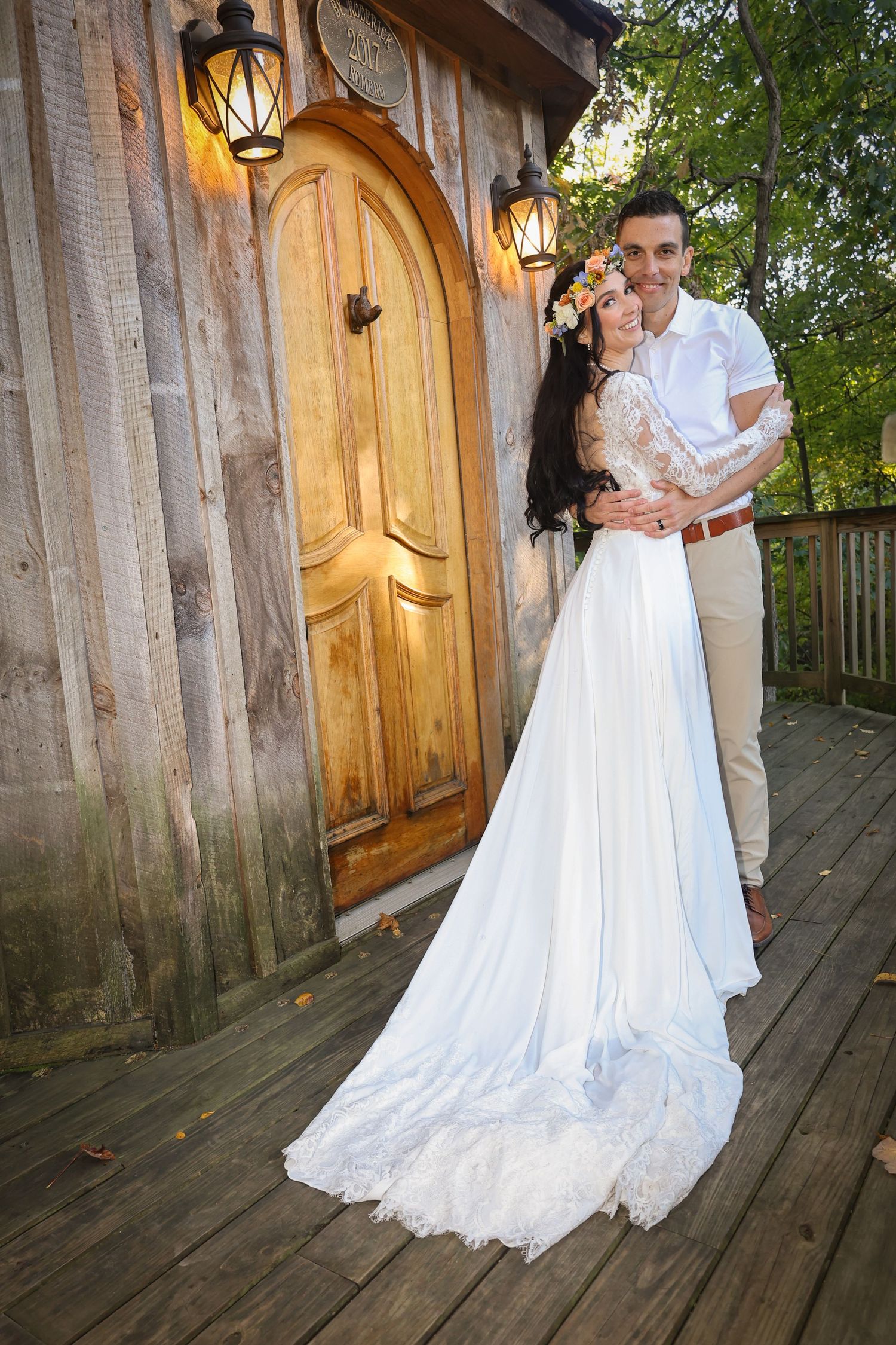 Romantic wedding photo of couple embracing by rustic wooden door with lanterns.