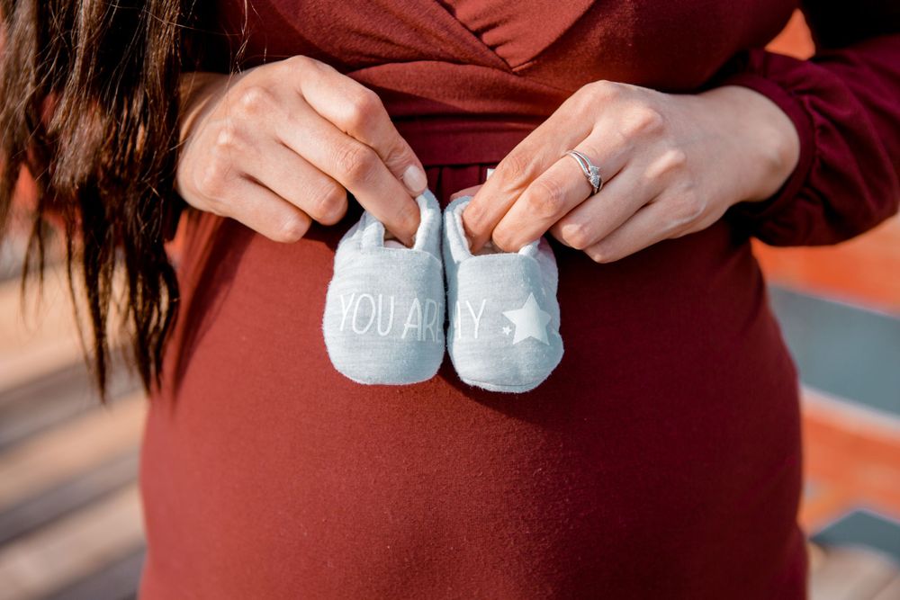 Close-up shots holding tiny baby shoes during maternity photo session.