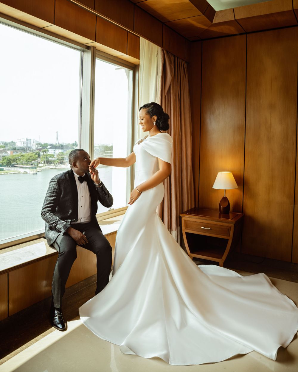 A romantic wedding photo featuring a flowing white dress and window view of a cityscape.